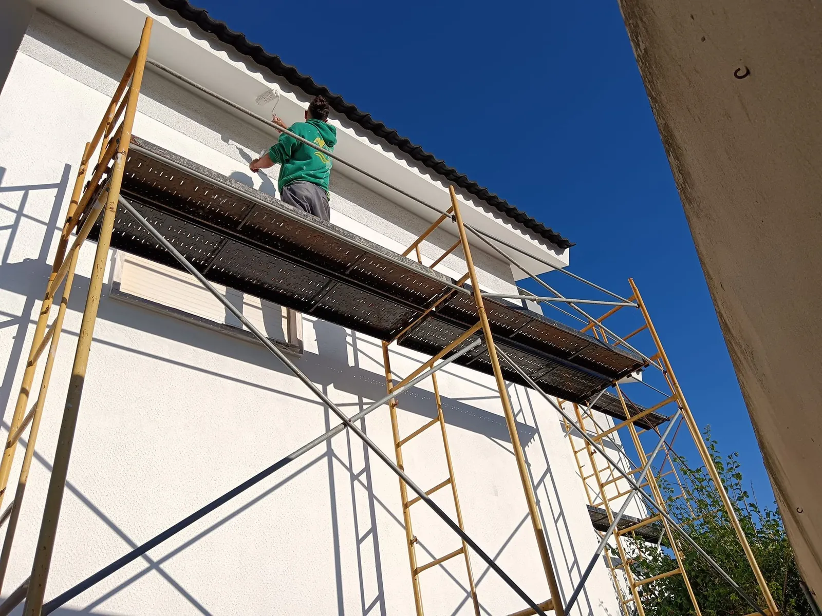 Profissional da Valter Almeida Soluções a pintar a fachada de uma moradia a partir de um andaime